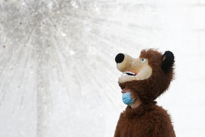 Un hombre con mascarilla y un disfrazado de oso, frente a una fuente en el centro de Kiev (Ucrania).