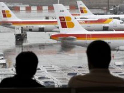 Dos pasajeros observan varios  aviones de la compa&ntilde;ia Iberia en las pistas del aeropuerto de Barajas.