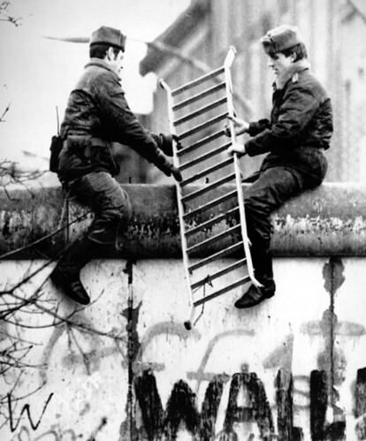 Dos guardas subidos sobre el Muro portan una escalera para pasarla al otro lado.