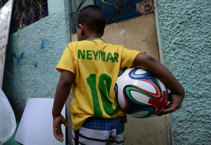 Un niño de la favela Jacarezinho camina con una pelota de fútbol tras la decoración de las calles y casas de la vecindad para el próximo Mundial de la FIFA, en Río de Janeiro. 