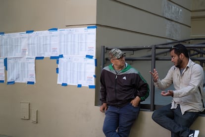 Dos hombres hablan junto a las listas de mesas de votación de la Universidad Tecnológica Nacional.