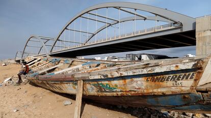 Un chico permanece sentado en un cayuco de pescadores junto a un puente a medio construir en Dakar, Senegal, el 13 de julio de 2020.