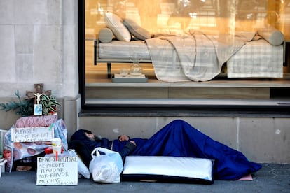 Un indigente duerme junto a un escaparate en el Paseo de Gracia de Barcelona 