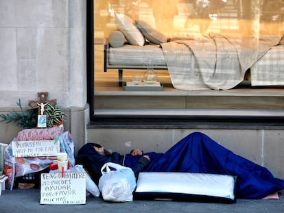 Un indigente duerme junto a un escaparate en el Paseo de Gracia de Barcelona