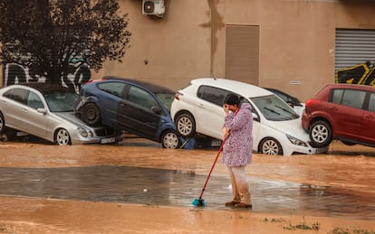 Una mujer realiza labores de limpieza junto a vehículos destrozados tras el paso de la dana por el barrio de La Torre de Valencia, el pasado 30 de octubre.