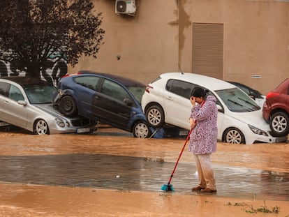 Una mujer realiza labores de limpieza junto a vehículos destrozados tras el paso de la dana por el barrio de La Torre de Valencia, el pasado 30 de octubre.