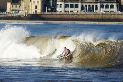 Un surfista sobre una ola en la playa gijonesa de San Lorenzo
