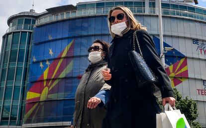 Dos mujeres caminan con máscaras de protección este jueves en Skopje, República de Macedonia del Norte, frente a la oficina de la UE, que mantiene una dedicatoria al país en su fachada tras aprobar un paquete de ayuda económica para la región.