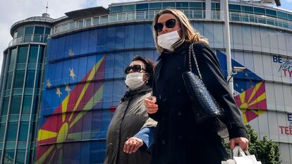 Dos mujeres caminan con máscaras de protección este jueves en Skopje, República de Macedonia del Norte, frente a la oficina de la UE, que mantiene una dedicatoria al país en su fachada tras aprobar un paquete de ayuda económica para la región.