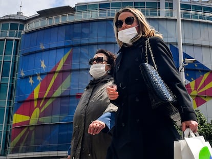 Dos mujeres caminan con máscaras de protección este jueves en Skopje, República de Macedonia del Norte, frente a la oficina de la UE, que mantiene una dedicatoria al país en su fachada tras aprobar un paquete de ayuda económica para la región.