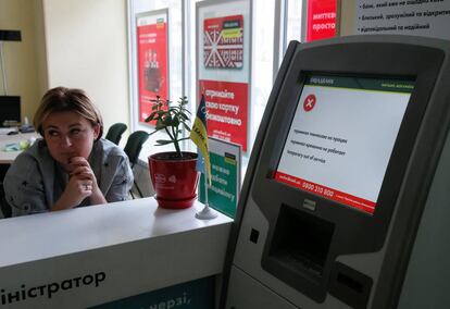 Una empleada de Oschadbank, junto a un cajero afectado por el virus, este martes en Kiev.