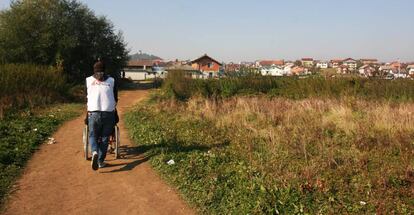 Un trabajador humanitario de Médicos sin Fronteras transporta a una persona en silla de ruedas en el camino de tierra que lleva de la explanada en Velika Kladusa donde se asientan los migrantes y refugiados a donde la ONG cuenta con una clínica móvil tres veces por semana.