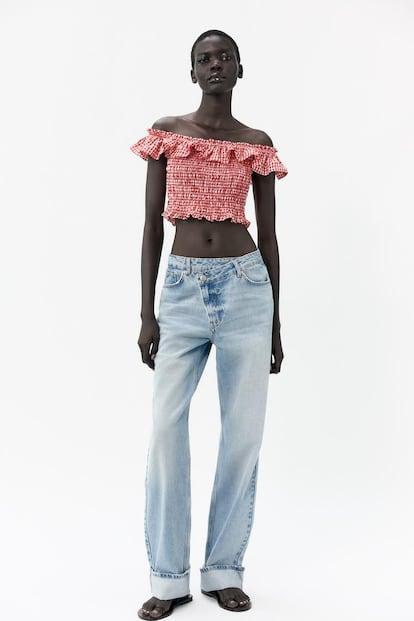 Zara presenta su oda al verano más 'naïf' con esta blusa de cuadros vichy y escote 'bardot' con volantes. El nido de abeja del cuerpo garantiza un ajuste cómodo y capaz de adaptarse a todo tipo de cuerpos. Una prenda para llevar desde ya con pantalones vaqueros amplios o bermudas. (22.95 euros). 