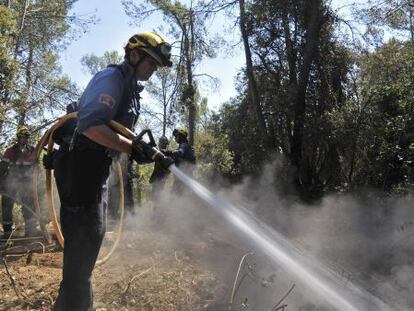 Un bombero remoja un &aacute;rea caliente del bosque afectado por el incendio de Madremanya.