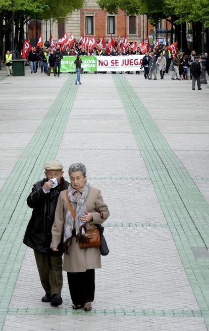 Dos pensionistas caminan delante de la pancarta que bajo el lema "con la sanidad y la educación no se juega", la Plataforma por la defensa del estado de bienestar ha exhibido hoy por las calles de Pamplona