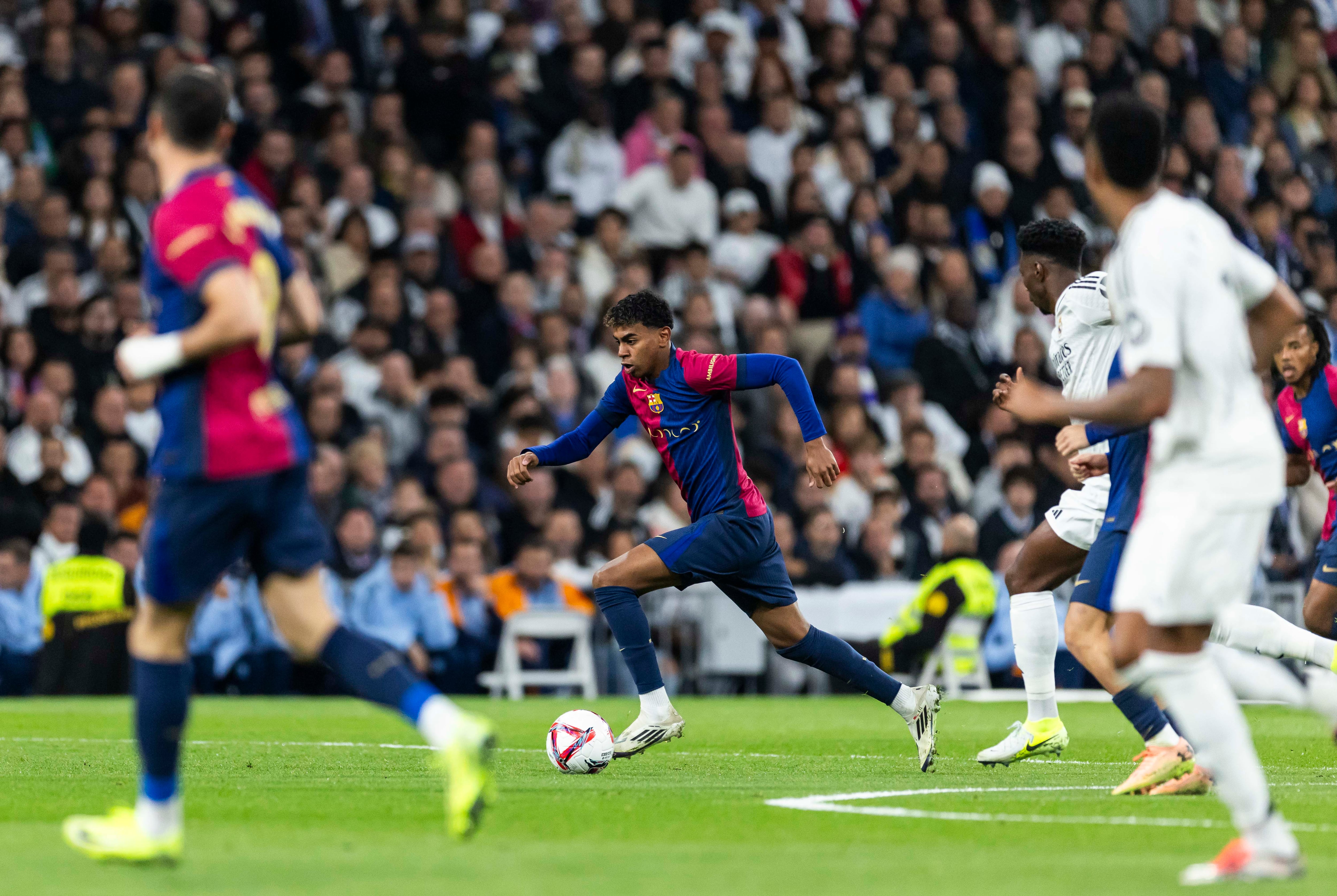 Lamine Yamal controla el balón perseguido por varios jugadores del Real Madrid.