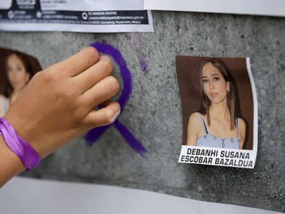 A woman attaches a purple ribbon on a wall with images of Debanhi Escobar, in San Nicolás de los Garza, Mexico.