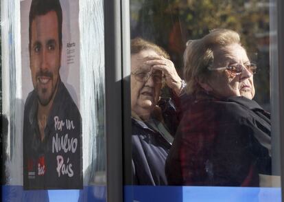 Dos mujeres esperan en una parada de autobús en La Vaguada con un cartel del candidato de IU a presidir el Gobierno, Alberto Garzón.