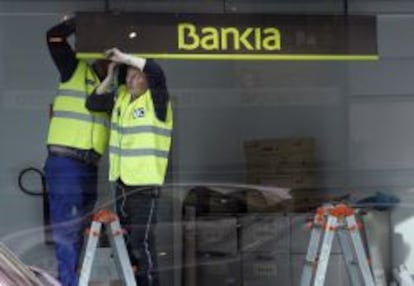 Dos operarios colocan el logotipo de Bankia en una sucursal