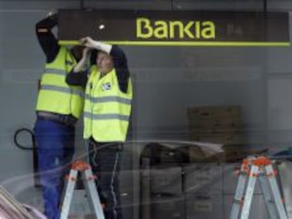 Dos operarios colocan el logotipo de Bankia en una sucursal