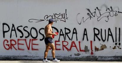Un hombre pasa ante un graffiti que reza: &quot;Passos a la calle, huelga general&quot;.