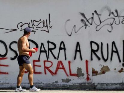 Un hombre pasa ante un graffiti que reza: &quot;Passos a la calle, huelga general&quot;.