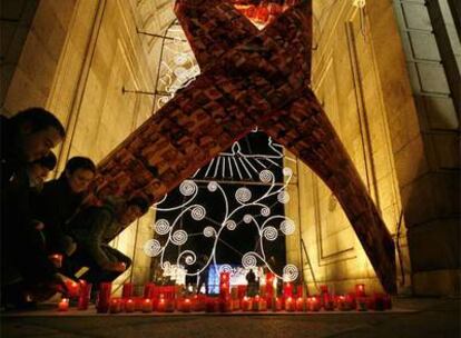 Un grupo de personas enciende velas bajo el lazo rojo colocado en la Puerta de Alcalá.