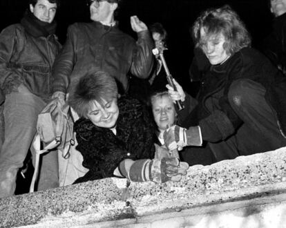Ciudadanos berlineses usan un martillo y un cincel para romper una de las secciones de la parte de arriba del muro de Berlín.