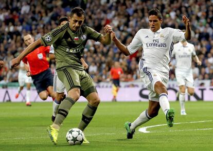 El centrocampista serbio del Legia Varsovia, Miroslav Radovic (i), dispara a puerta ante la oposición del defensa francés del Real Madrid, Raphael Varane (d), durante el partido de Liga de Campeones disputado en el estadio Santiago Bernabéu.