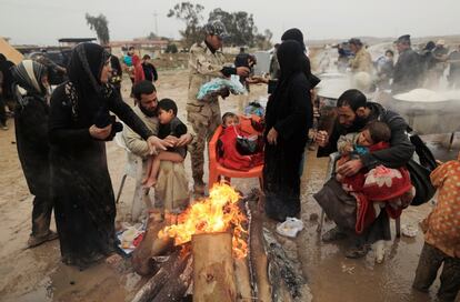 Un grupo de desplazados iraquíes se calienta alrededor de una hoguera en el punto de 'Hashid Shaabi', también conocido como punto de movilización popular, después de abandonar sus hogares mientras las fuerzas iraquíes se enfrentan al Estado Islámico, en Mosul.