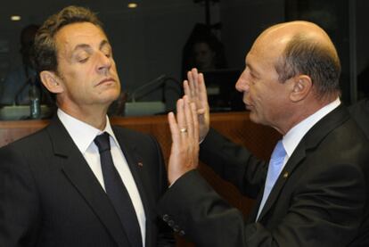 Sarkozy escucha al presidente rumano, Traian Basescu, durante la cumbre europea de ayer en Bruselas.