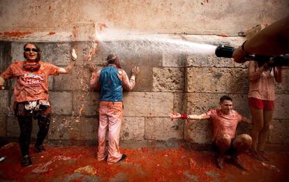 Juerguistas cubiertos de pulpa de tomate son lavados con una manguera durante la Tomatina, en Buñol (Comunidad Valenciana).