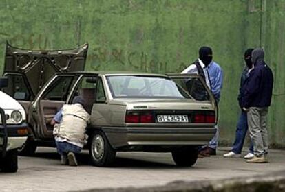 Agentes de la <i>ertzaintza</i> inspeccionan al coche del guarda jurado en el que ha sido colocada una bomba lapa.