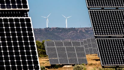 Un parque de energía fotovoltaica, en Tarragona, con dos aerogeneradores al fondo.