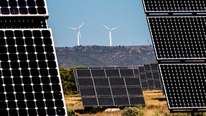 Un parque de energía fotovoltaica, en Tarragona, con dos aerogeneradores al fondo.