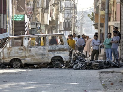 Varias personas observan veh&iacute;culos quemados durante la protesta de la casta jat en el estado de Haryana, India, el 21 de febrero.