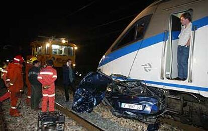 Bomberos observan los restos del vehículo en el que falleció su ocupante bajo el morro del tren Alaris.