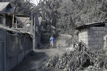 Los terremotos han causado grietas y fisuras en quince poblaciones próximas al Taal y tres carreteras en la provincia de Batangas, por lo que se han instalado controles militares por motivos de seguridad en numerosos accesos. En la imagen, un residente camina el martes 14 de enero junto a viviendas y árboles dañados por las cenizas volcánicas en Laurel (Filipinas).