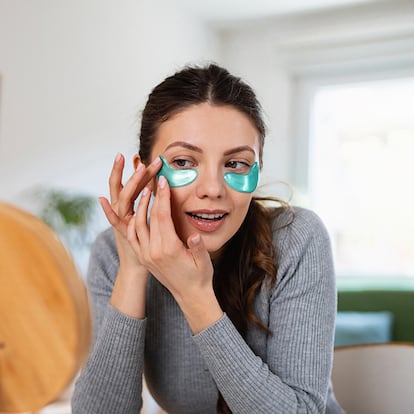 Una chica poniéndose los parches para debajo de los ojos en el salón de su casa frente a un pequeño espejo