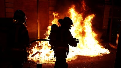 Dos bomberos junto a un contenedor en llamas, en el centro de Madrid este sábado. 