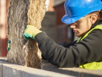 Un trabajador de la construcción coloca una manta de aislamiento térmico en la cavidad de un muro.