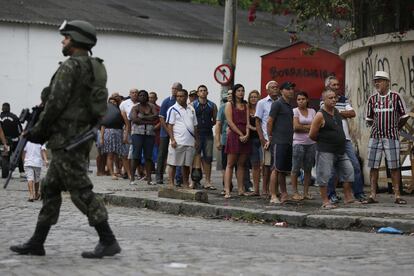 Um soldado do Exército reforça a segurança no Rio de Janeiro e patrulha uma rua em frente a um colégio do Complexo da Maré, enquanto os eleitores aguardam na fila para votar.