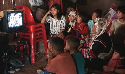 Una mujer de la etnia akha vestida a la manera tradicional ve una telenovela en su casa de Doi Tung, en Tailandia, acompañada de sus hijos.