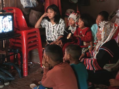 Una mujer de la etnia akha vestida a la manera tradicional ve una telenovela en su casa de Doi Tung, en Tailandia, acompañada de sus hijos.