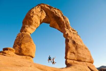 Dois saltitantes excursionistas sob o Delicate Arch, em Utah (Estados Unidos).