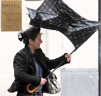 Una mujer en dificultades con su paraguas como consecuencia de las fuertes rachas de viento que azotan el norte de la Penínnsula debido al temporal.