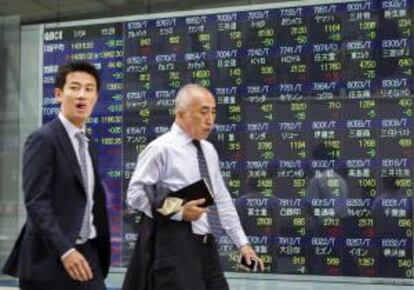 Dos viandantes pasan por delante de una pantalla con los resultados de la bolsa de Tokio. EFE/Archivo