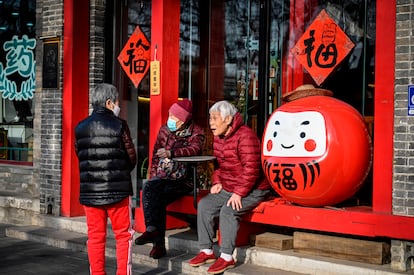 Varias personas mayores conversan en el exterior de un restaurante en una calle de Pekín.