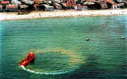 Una embarcación rodea y limpia una de las manchas de petróleo  frente a las playas de Salou.