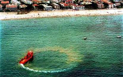 Una embarcación rodea y limpia una de las manchas de petróleo frente a las playas de Salou.